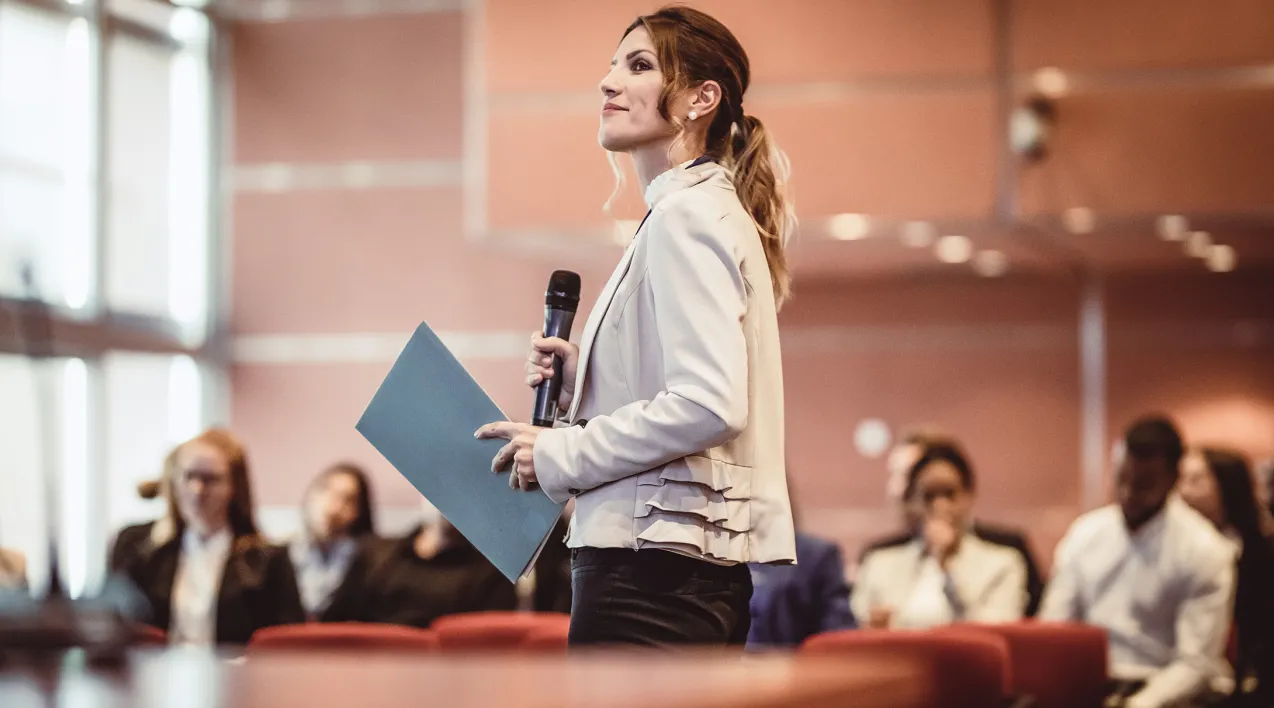 A woman stands in front of an audience at a conference.