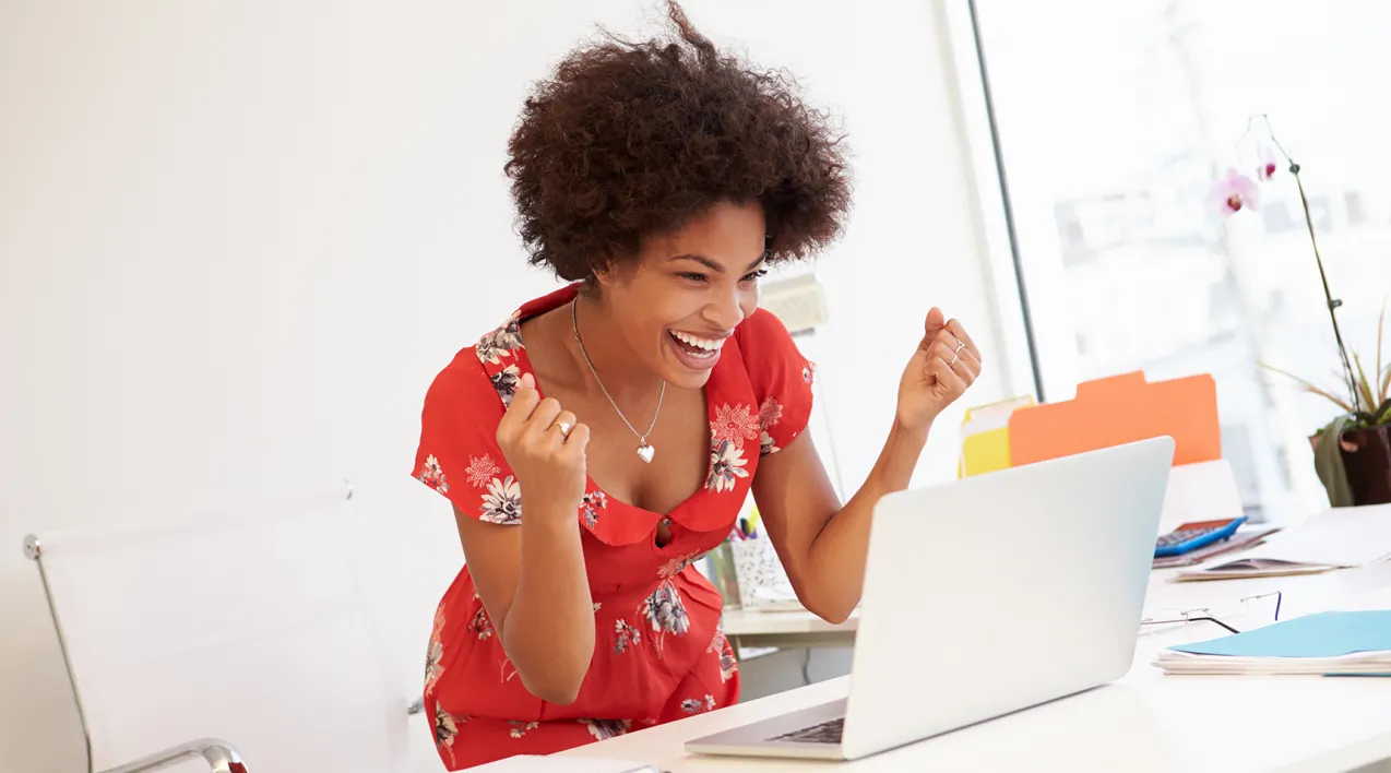 A woman celebrates a success at a computer desk.