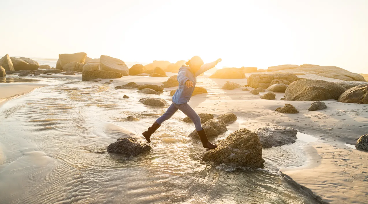 A woman jumps between rocks as the tide comes in.