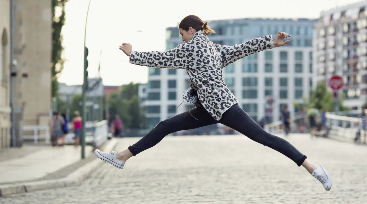 A woman leaps on a cobblestone road.