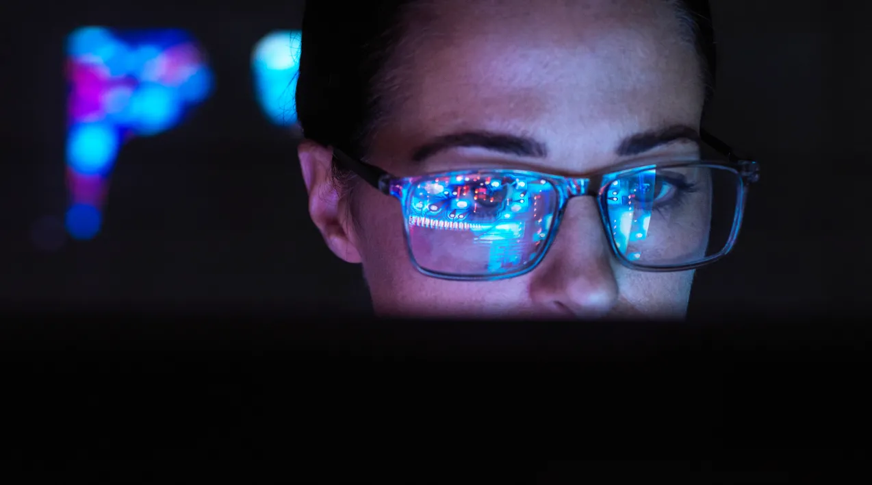 A woman in a dark room looking at a computer monitor.